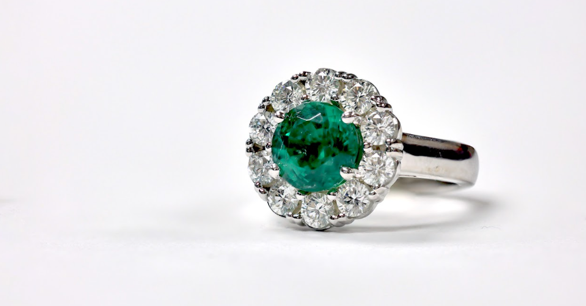 A silver-toned ring against a white background features a green center stone encircled by diamonds in a halo setting.