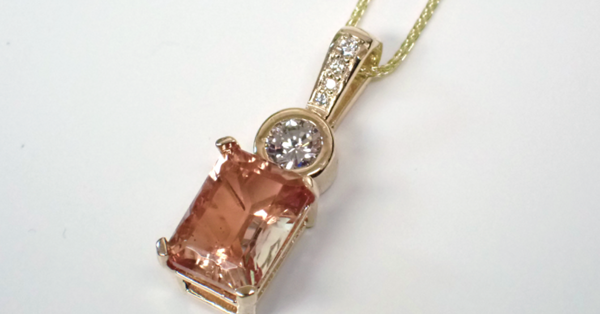 A gold necklace features a round clear stone and several smaller stones set above a rectangular peach-colored gemstone.