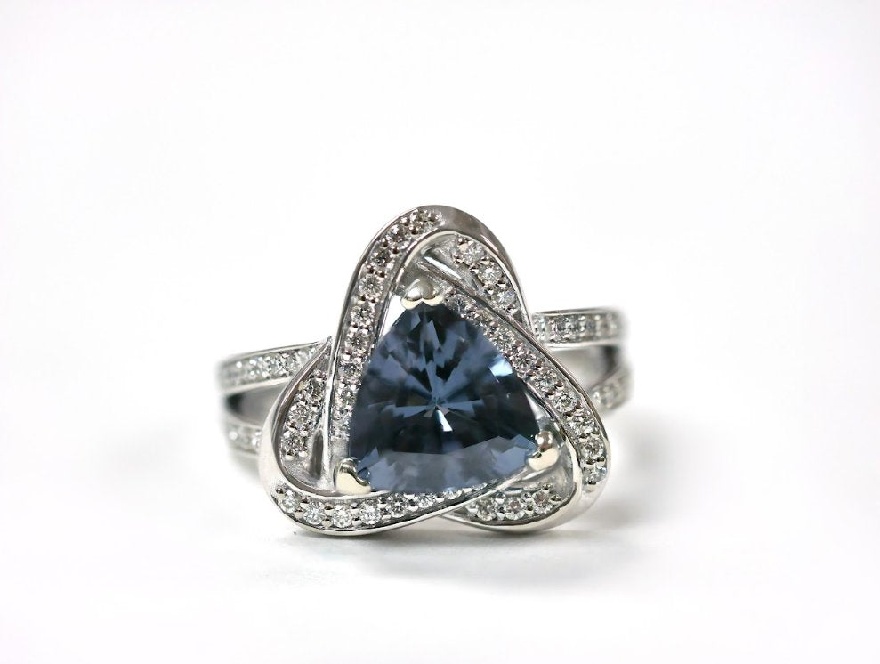 A silver-toned ring features a blue-gray triangular-cut gemstone set in three prongs and surrounded by diamonds.